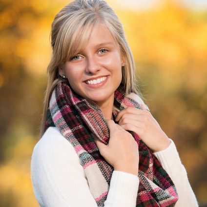 A woman is wearing a plaid scarf around her neck and smiling.