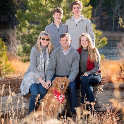 A family is posing for a picture with their dog while sitting on a log.