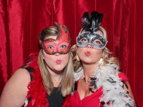 Two women wearing masks and feathers are posing for a picture in a photo booth.