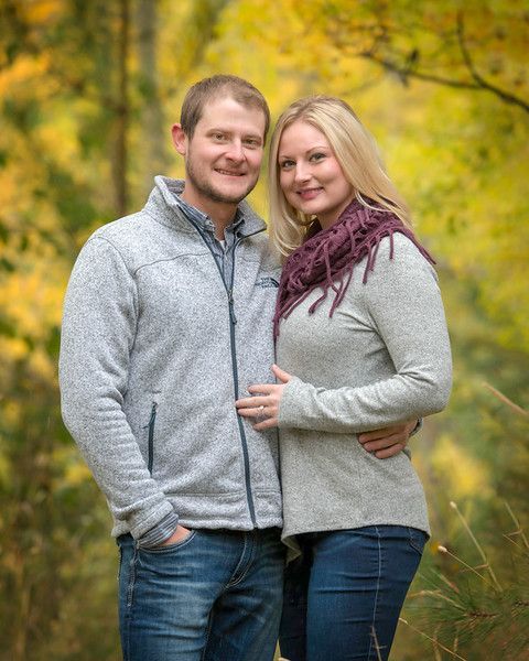 A man and a woman are posing for a picture in the woods.