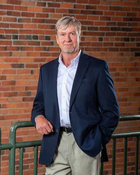 A man in a suit is standing in front of a brick wall.