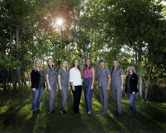 A group of women in scrubs are posing for a picture in front of trees.