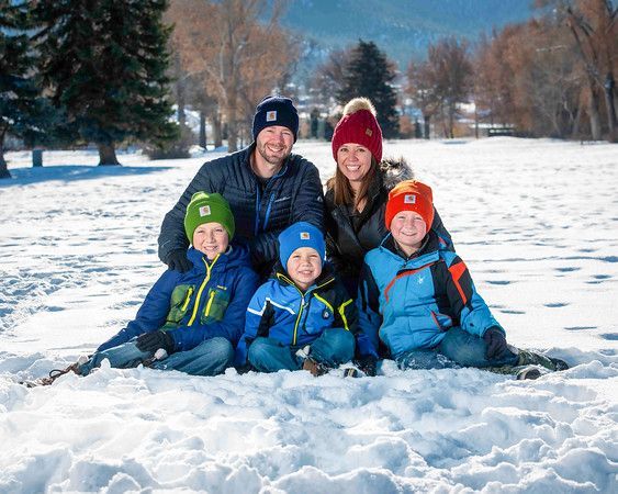 Three young boys are sitting in the snow wearing hats.