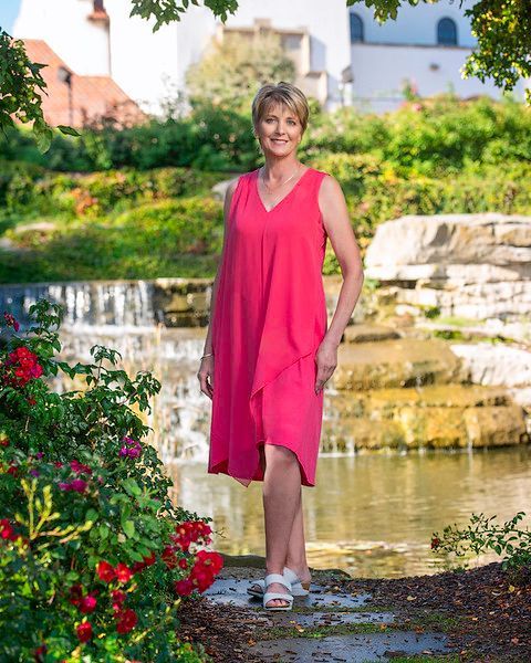 A woman in a pink dress is standing in front of a waterfall.