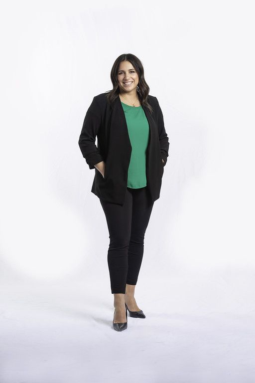 A woman in a green shirt and black pants is standing with her hands in her pockets.