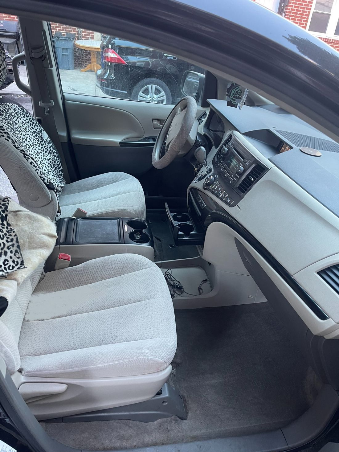 Interior of a minivan. Front seats are beige with leopard print covers. Dashboard and steering wheel visible.