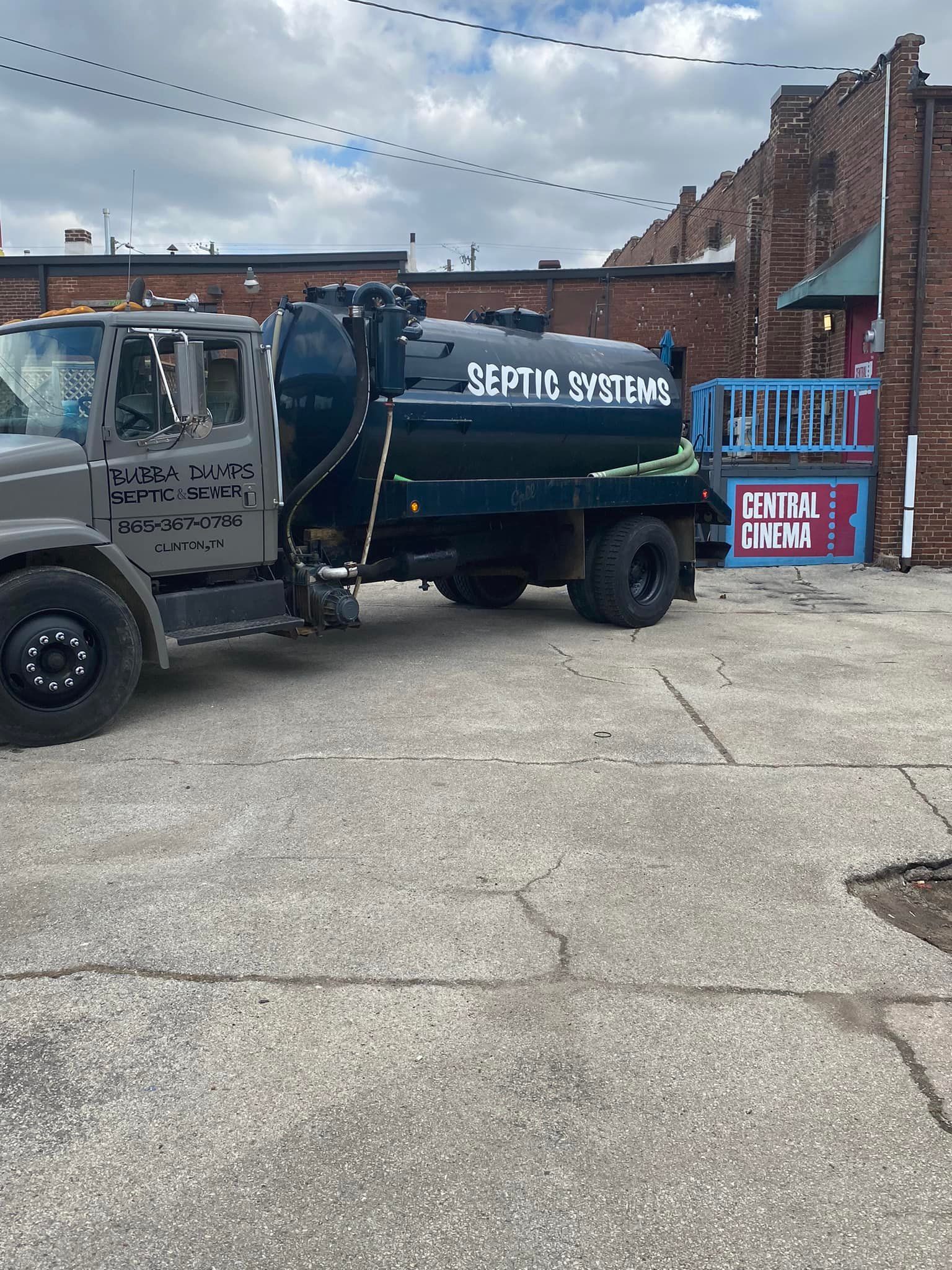 A septic tank truck is parked in a parking lot in front of a brick building.