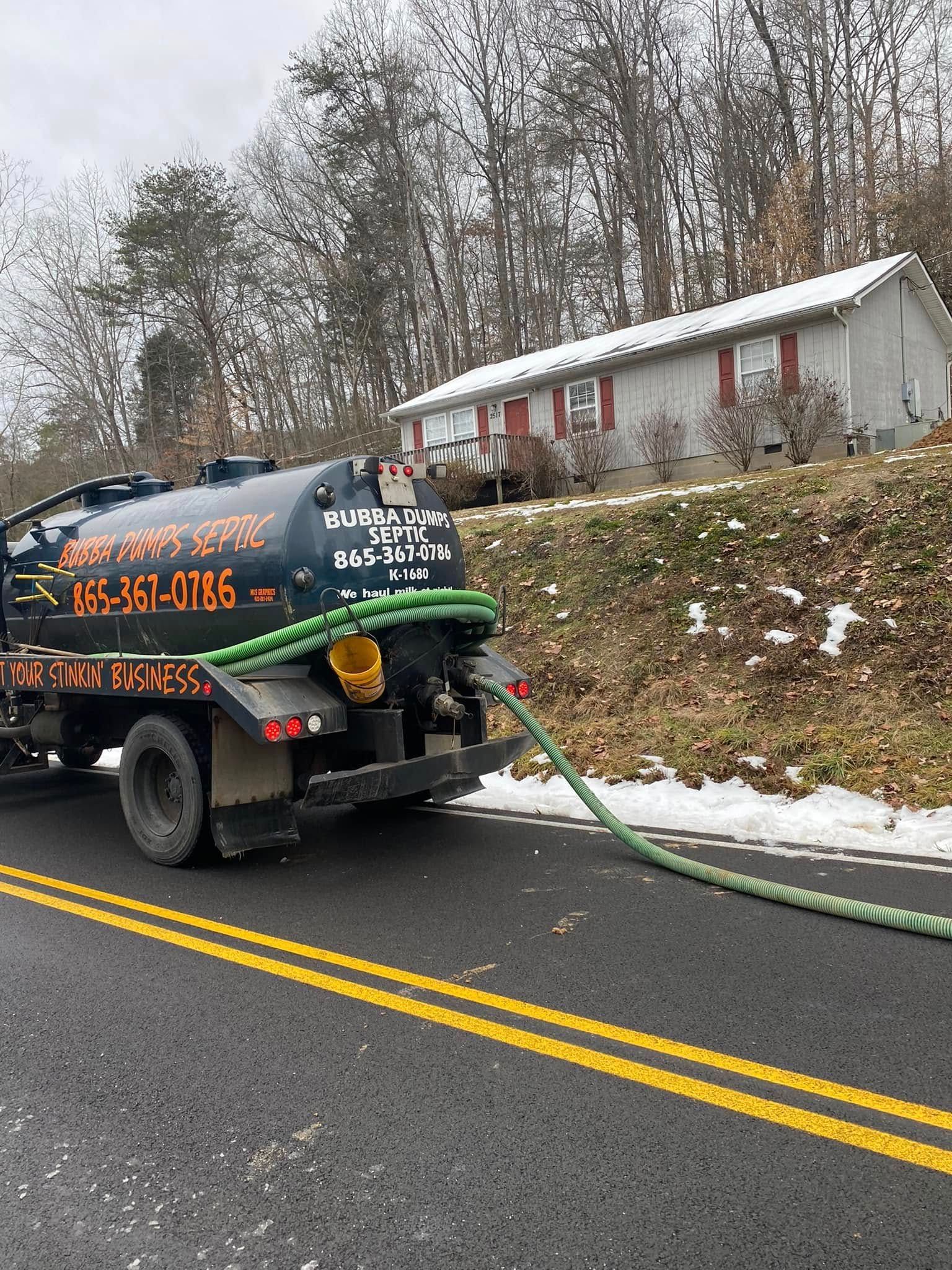 A septic tank truck is driving down a road next to a house.
