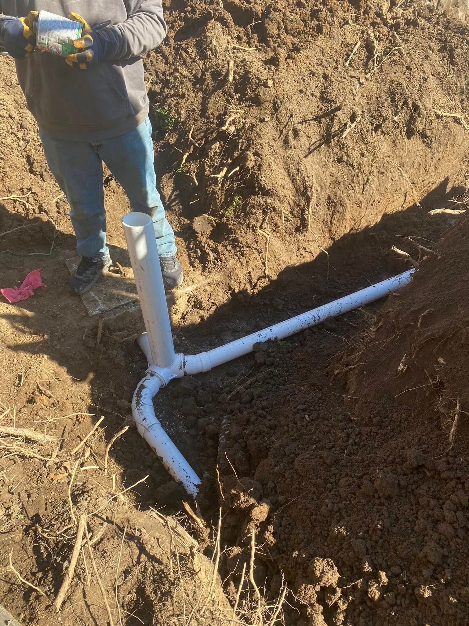 A man is standing in the dirt next to a pipe.