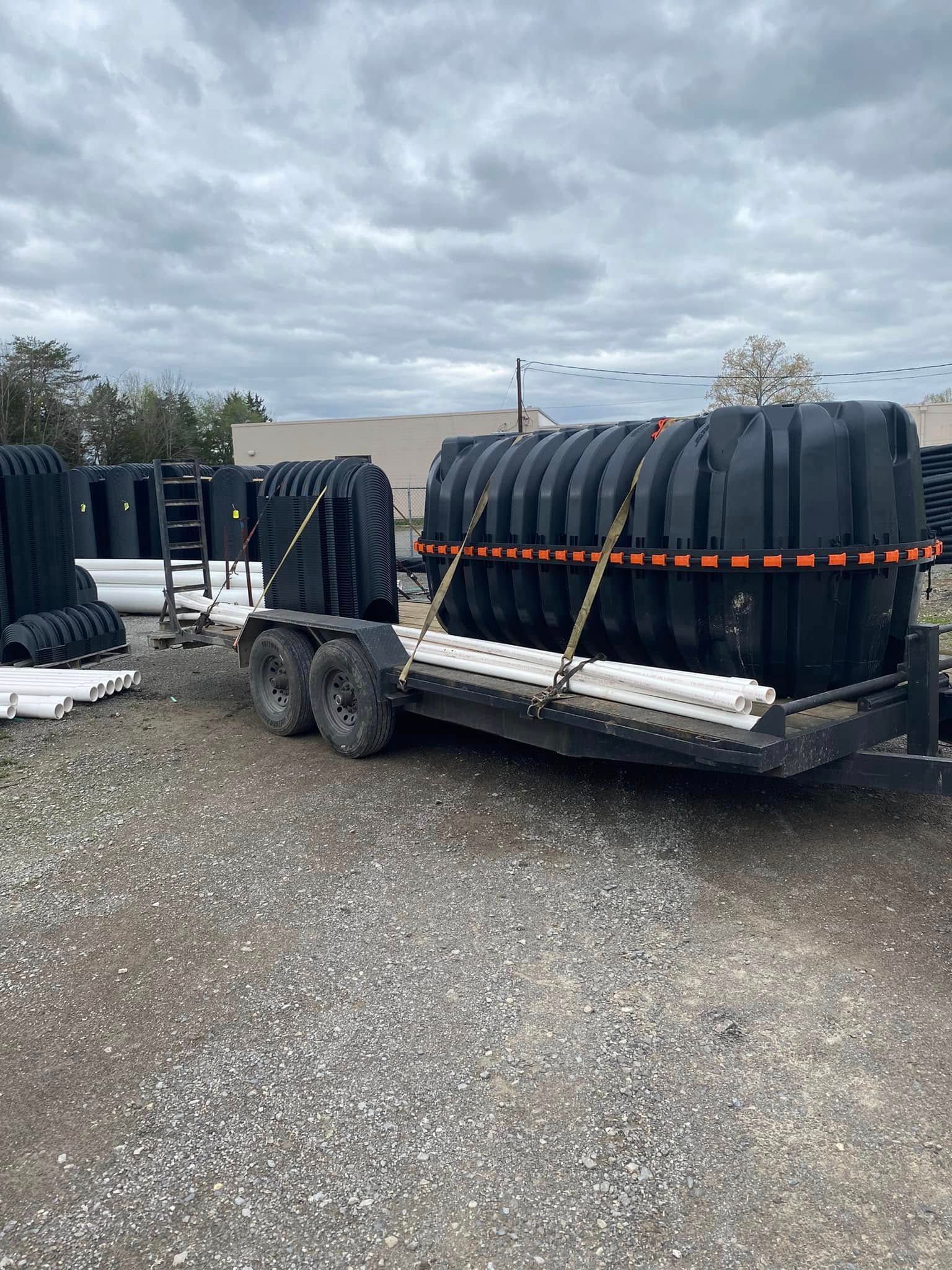 A trailer with a large black tank on it is parked in a gravel lot.