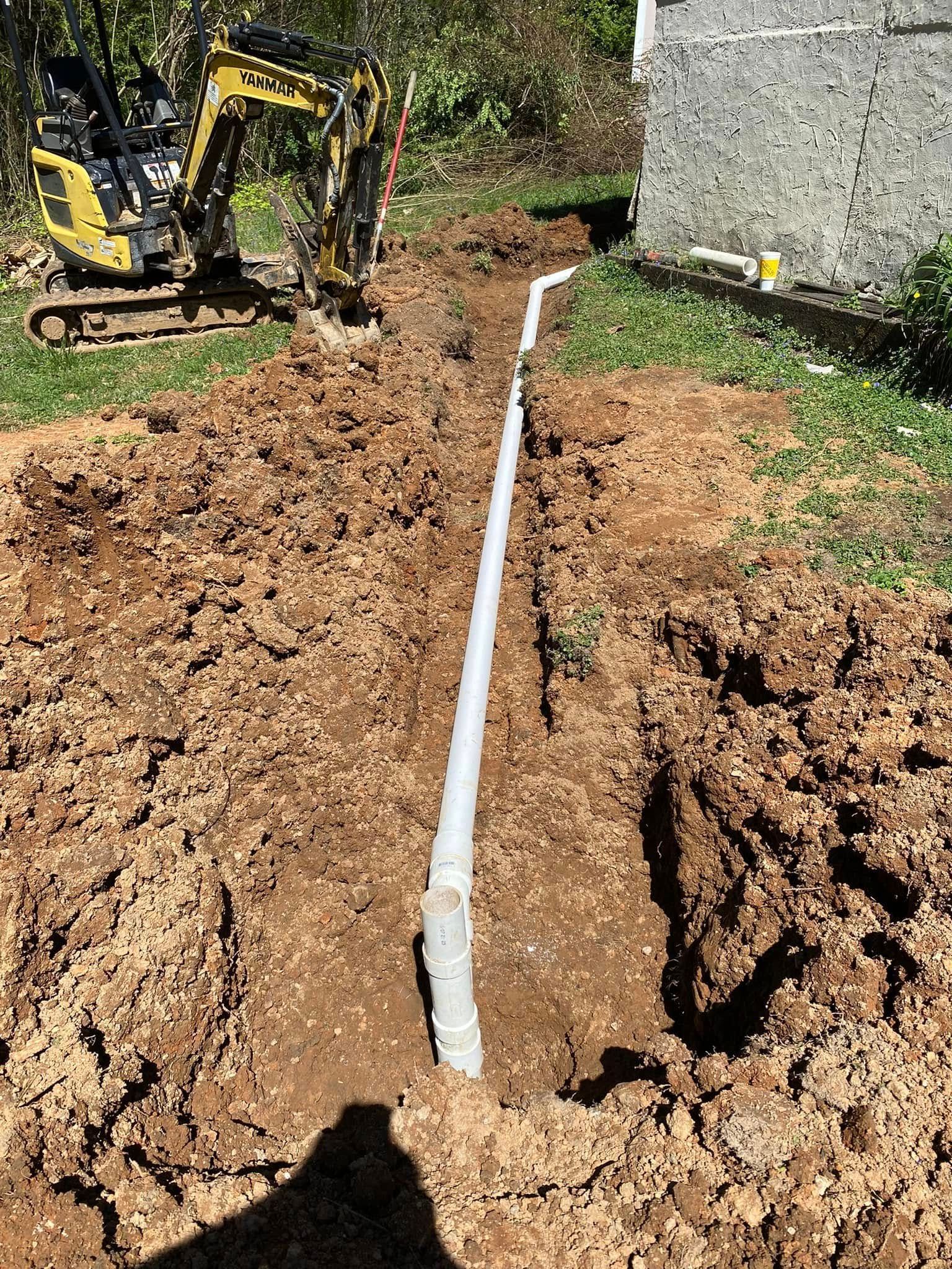 A pipe is being installed in the dirt next to a yellow excavator.