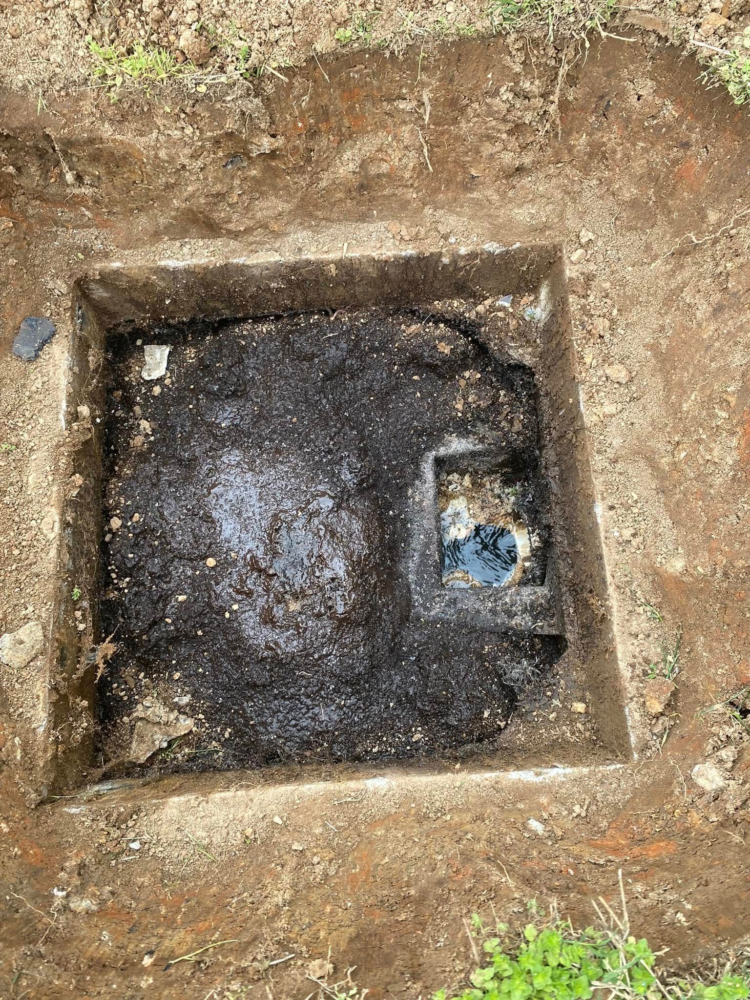 A square hole in the ground with a drain in it.