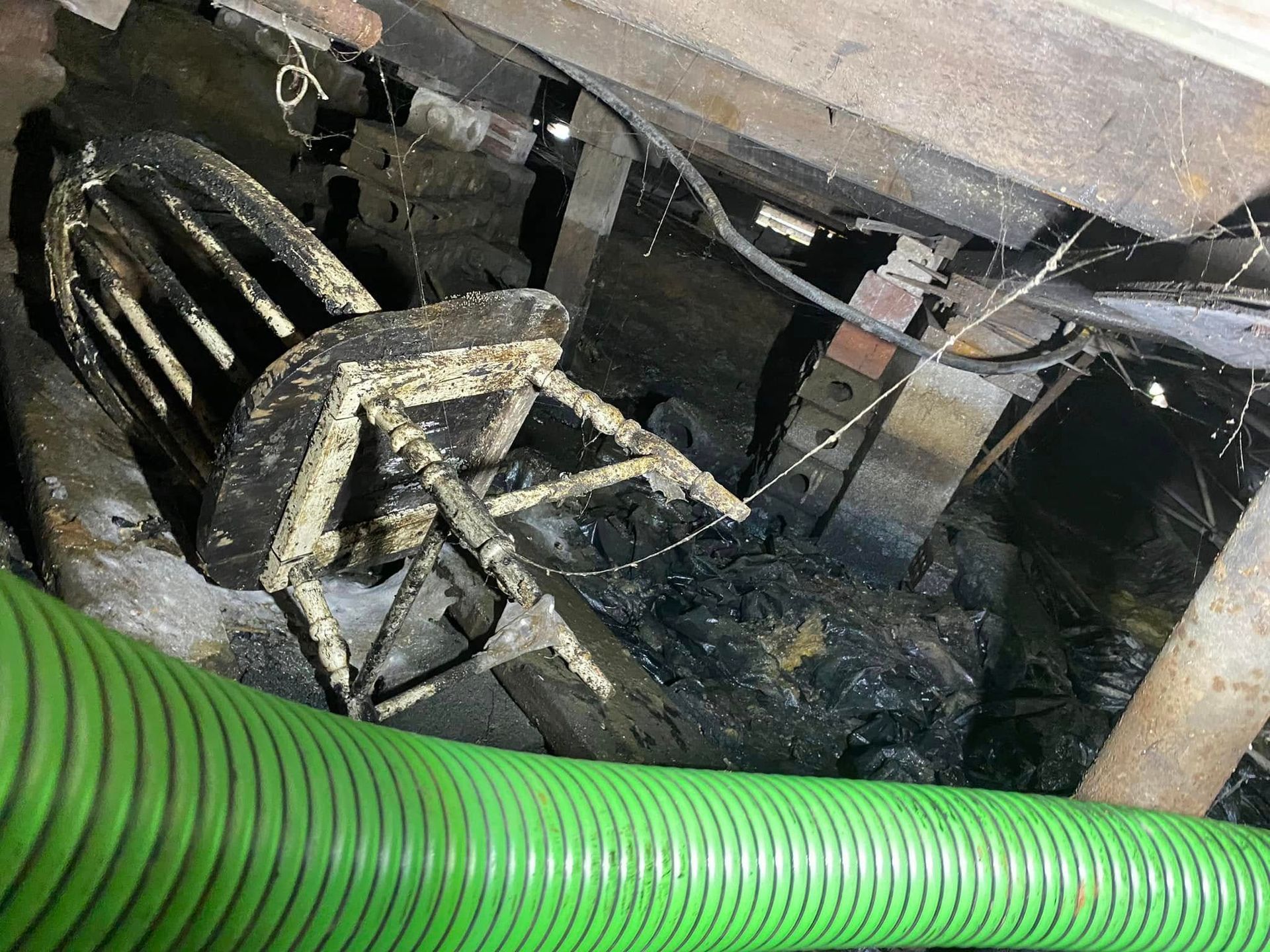 A green hose is sitting next to a chair in a dark room.