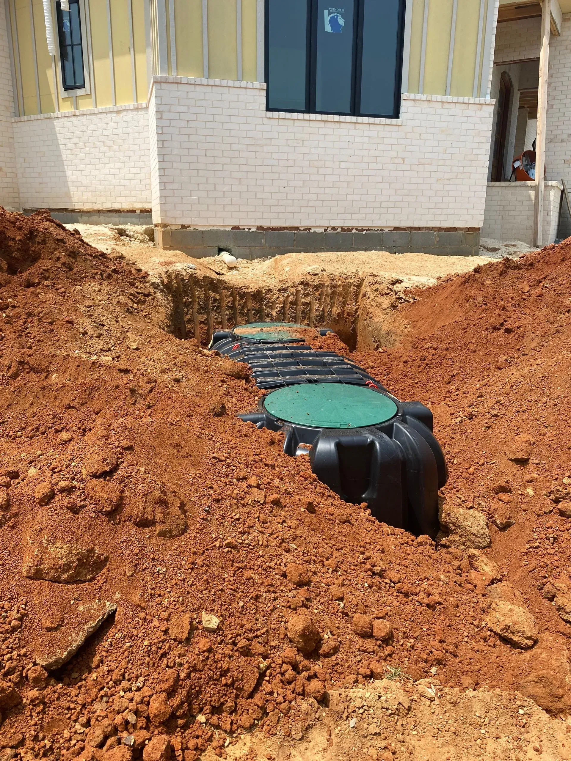 A septic tank is being installed in the dirt in front of a house.