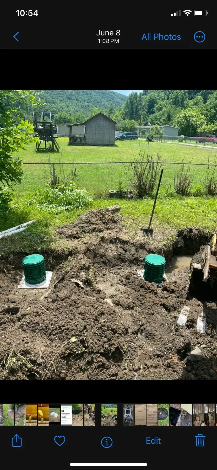 A phone screen shows a picture of a septic system being installed in a yard.