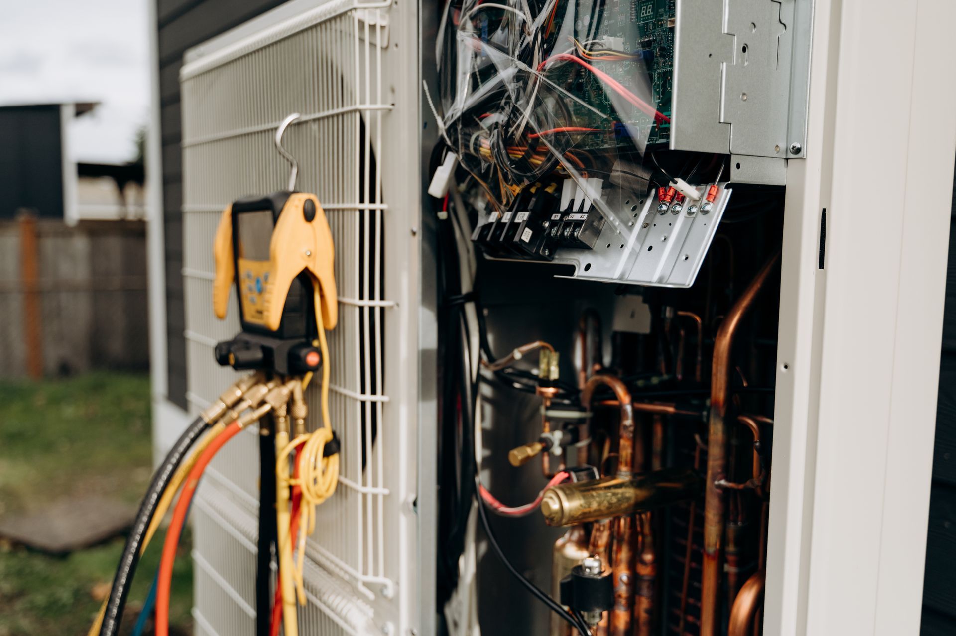 Open air conditioning unit with wires and copper pipes, yellow multimeter attached, outdoors.
