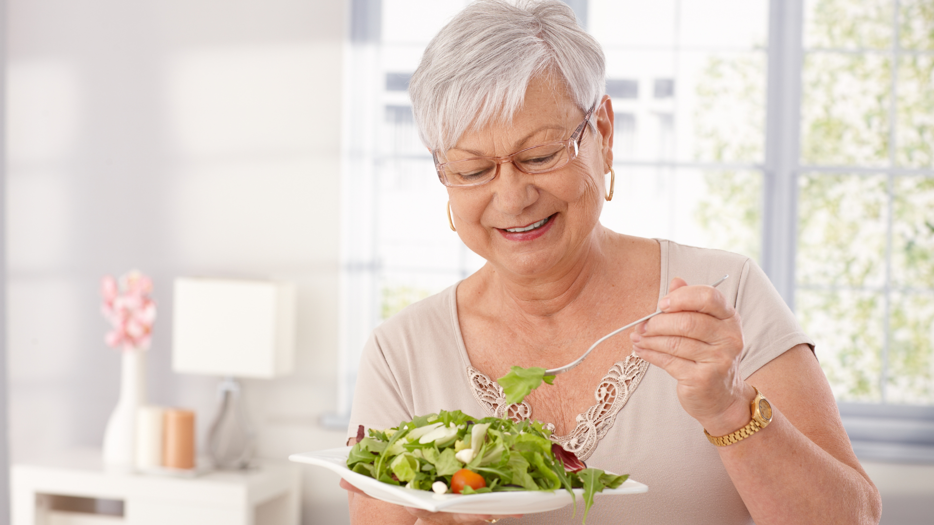 An elderly woman is eating a salad with a fork.