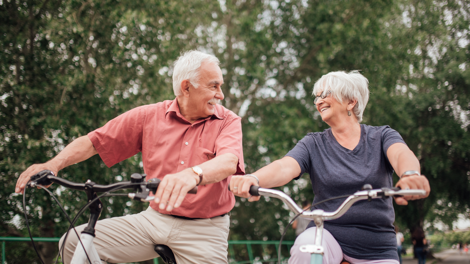 An elderly couple is riding bicycles together in a park. An elderly couple is riding bicycles together in a park.