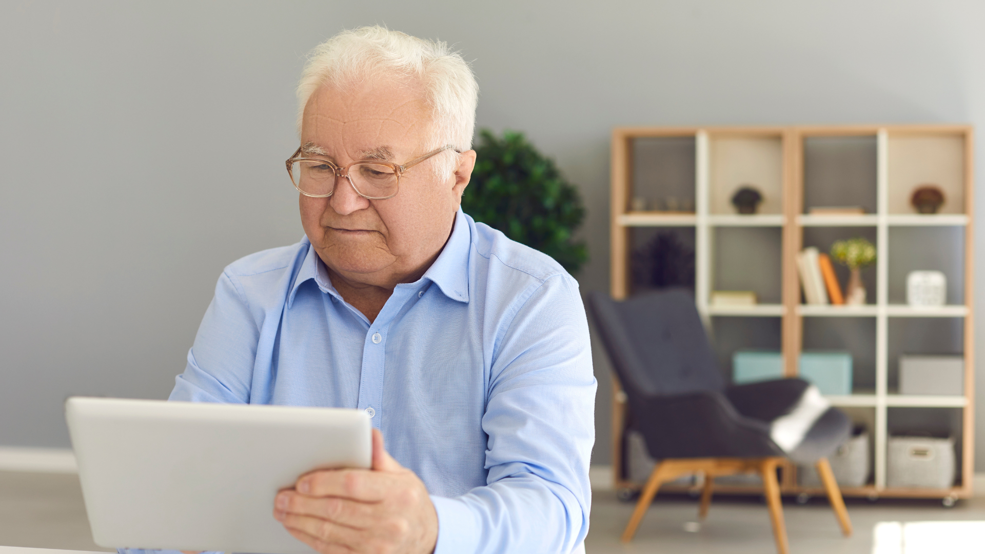 An elderly man is sitting at a table using a tablet computer. An elderly man is sitting at a table using a tablet computer.