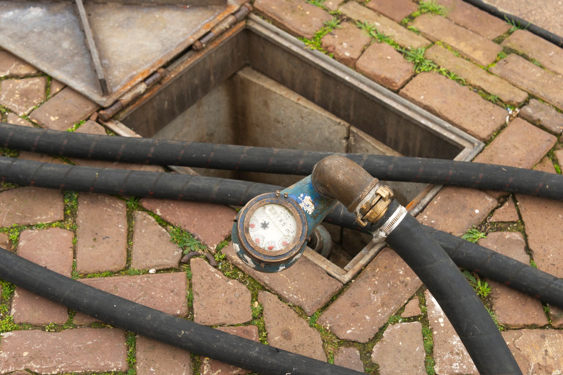 A hose is connected to a manhole cover on a brick sidewalk – Seguin, TX – 5J Plumbing