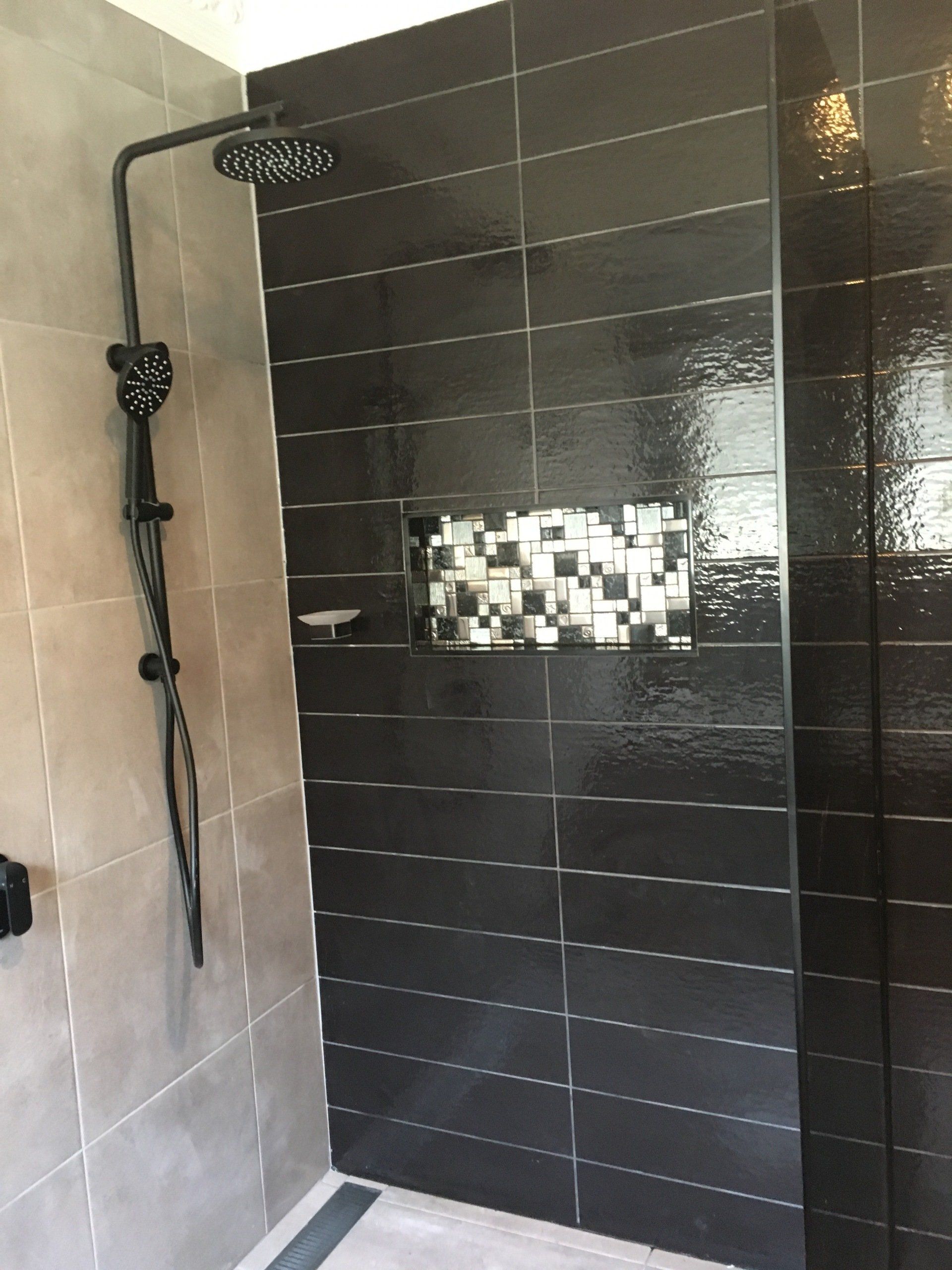 A shower with black tiles and a black shower head.