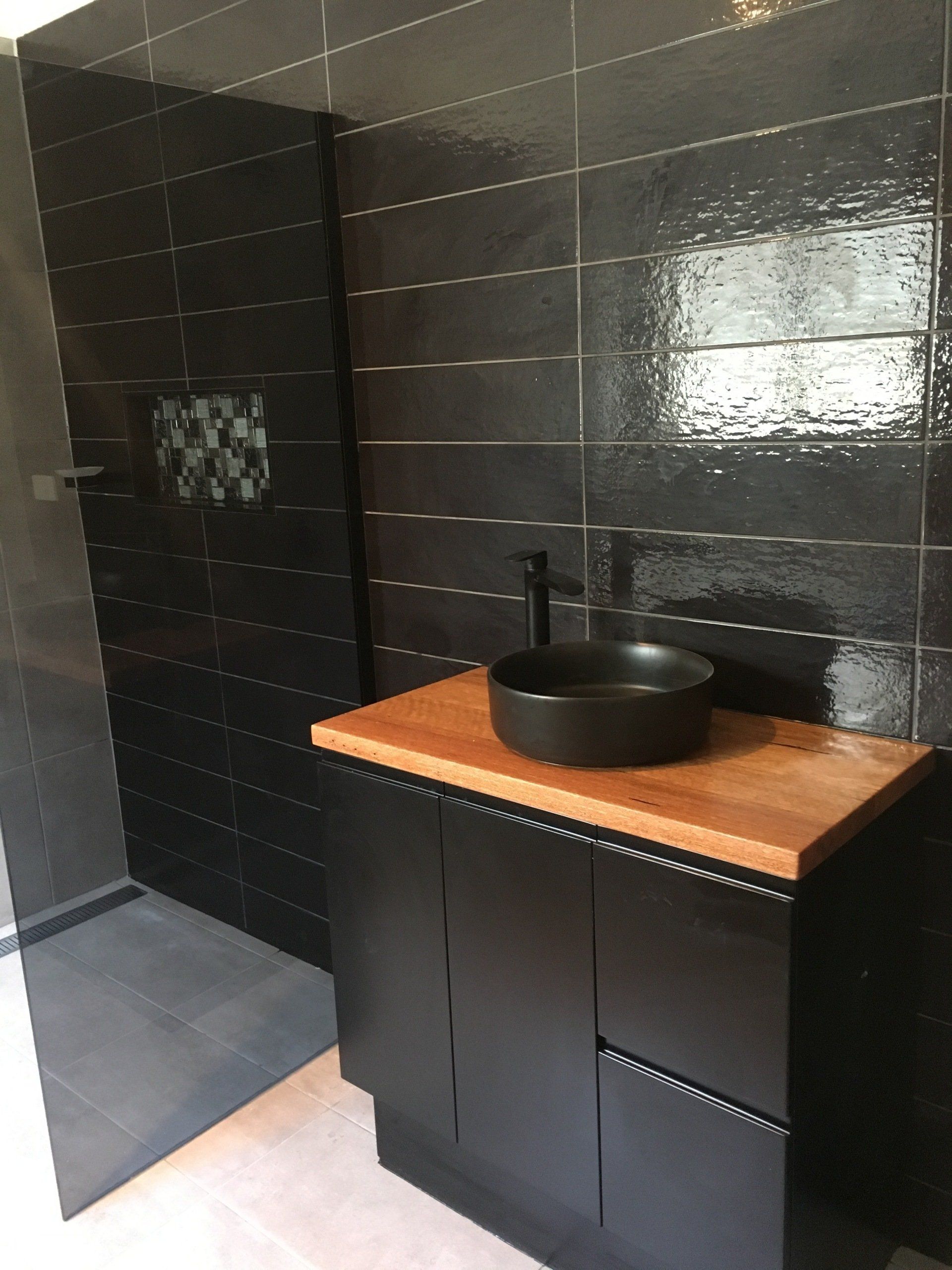 A bathroom with black tiles and a black sink