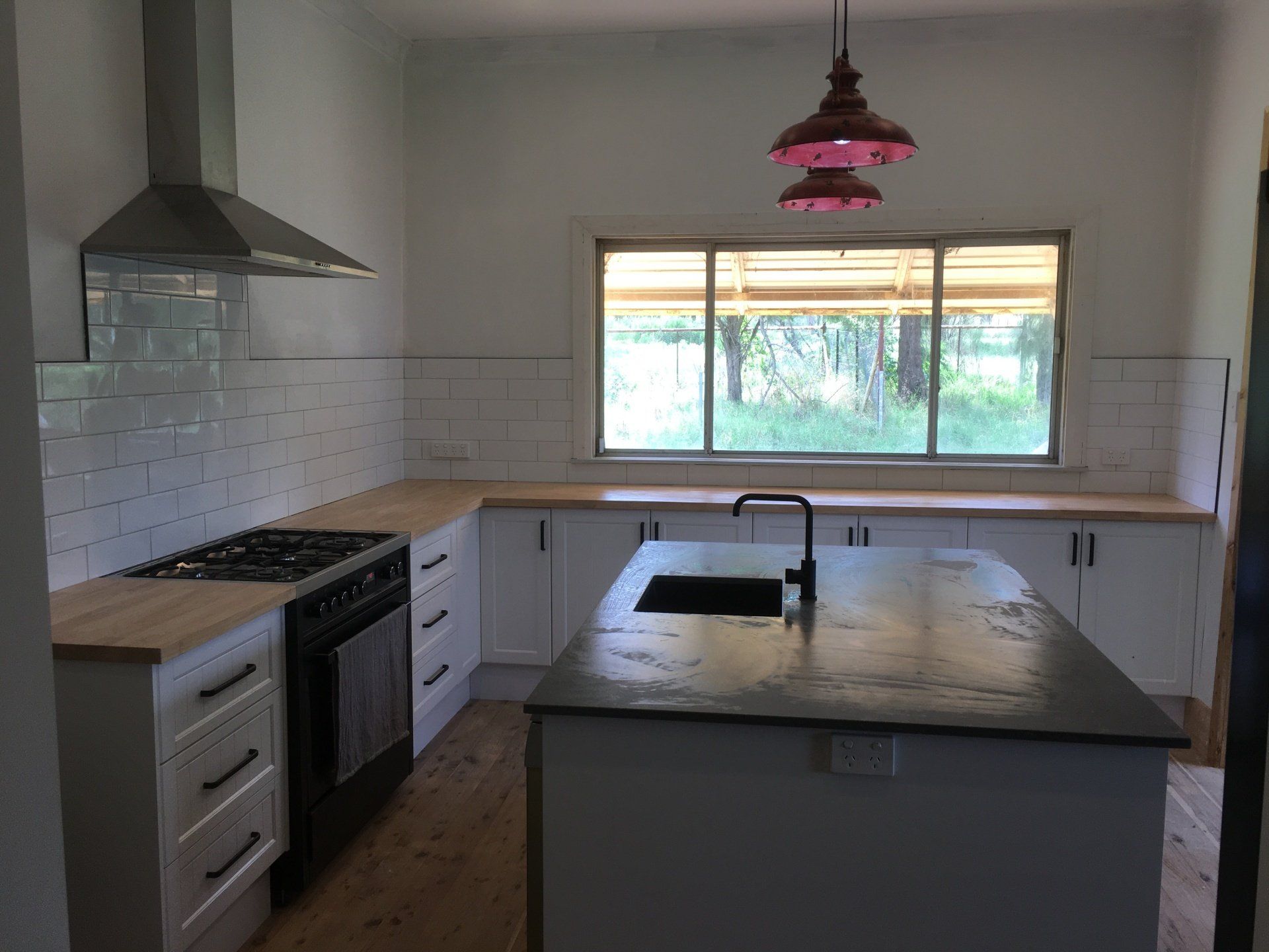 A kitchen with white cabinets , a stove , a sink and a window.