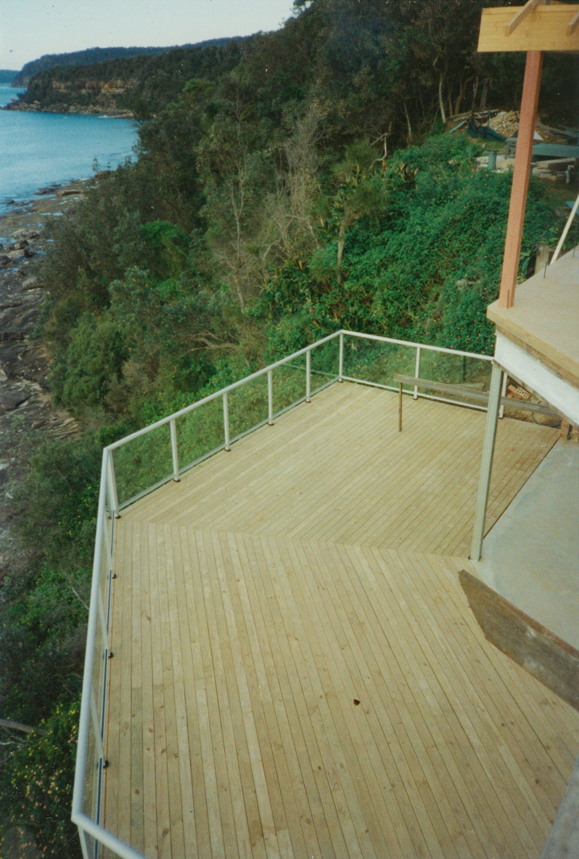 A wooden deck with a glass railing overlooking a body of water