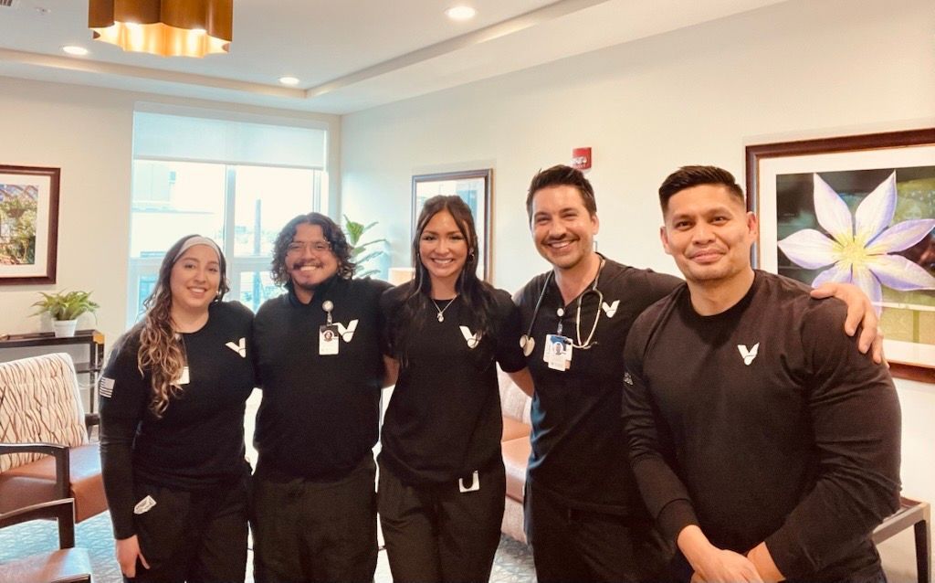 Group of five healthcare workers smiling in a well-lit room.