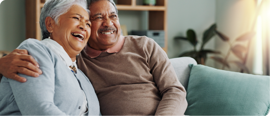 An elderly couple is sitting on a couch and laughing.