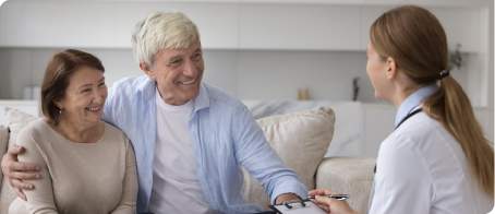 An elderly couple is sitting on a couch talking to a doctor.