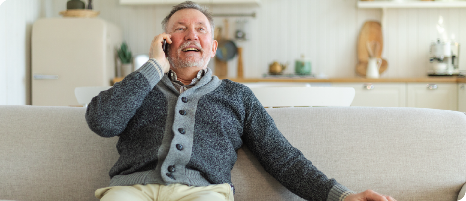 An elderly man is sitting on a couch talking on a cell phone.