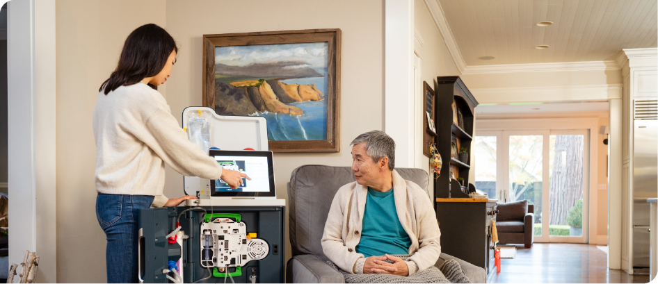 A woman is standing next to a man sitting in a chair in a living room.