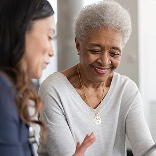 A woman is talking to an older woman while looking at a tablet.