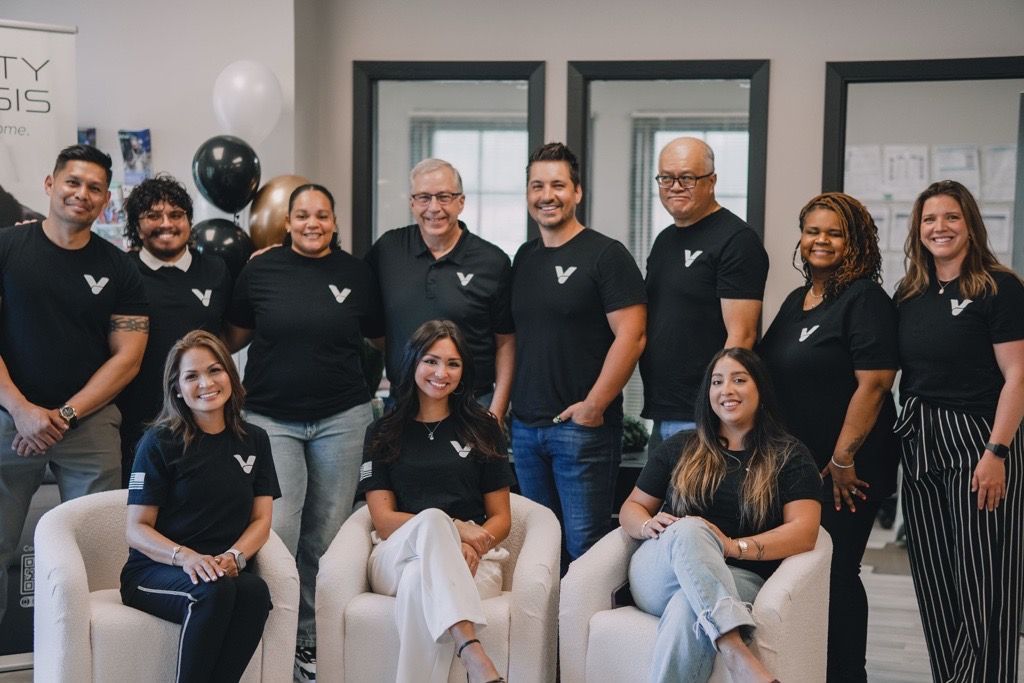 Group photo of a diverse team in black shirts with a white logo. They are smiling in a bright office.