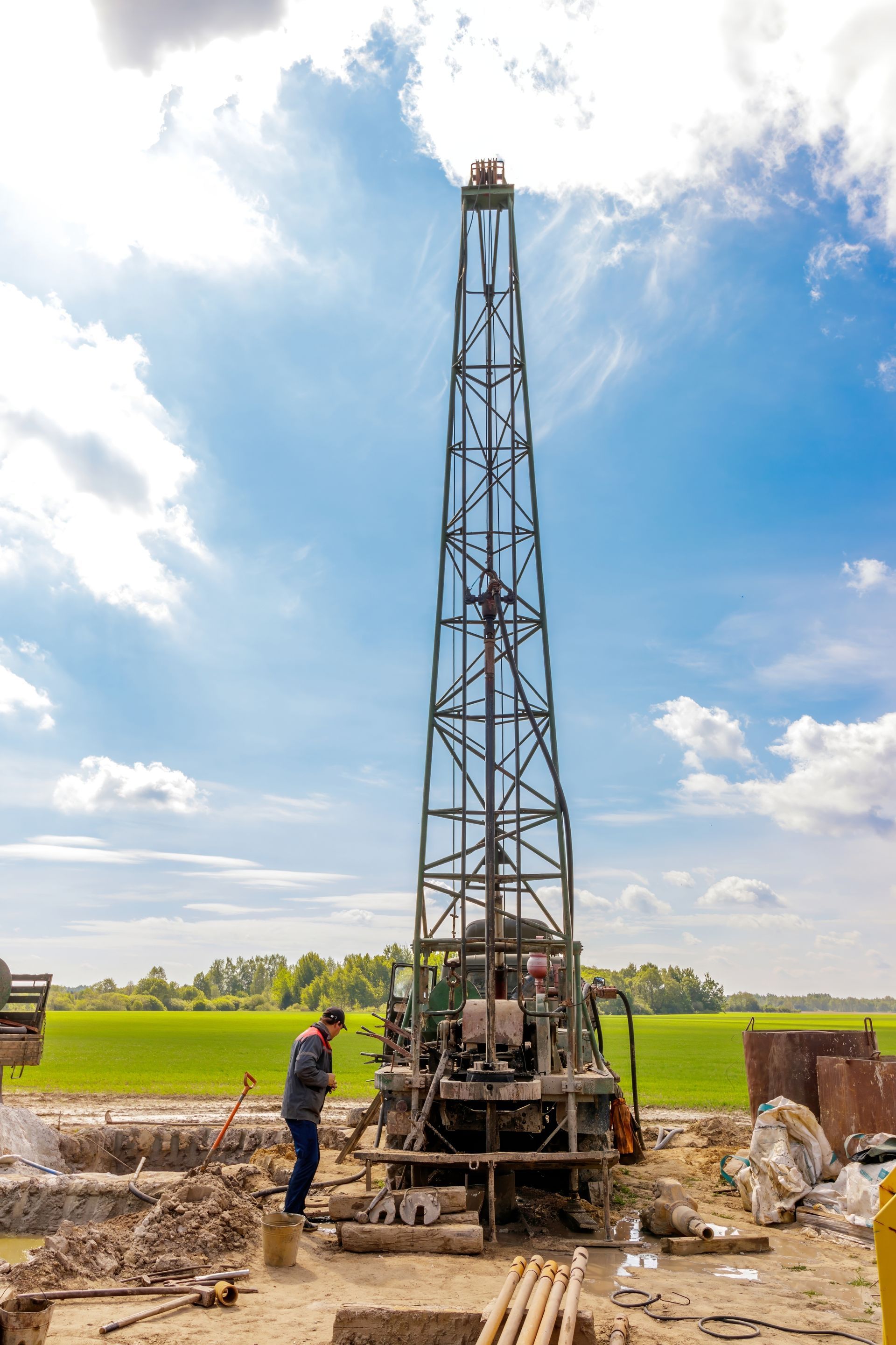 Drilling rig tower with worker, field in background, sunny sky.