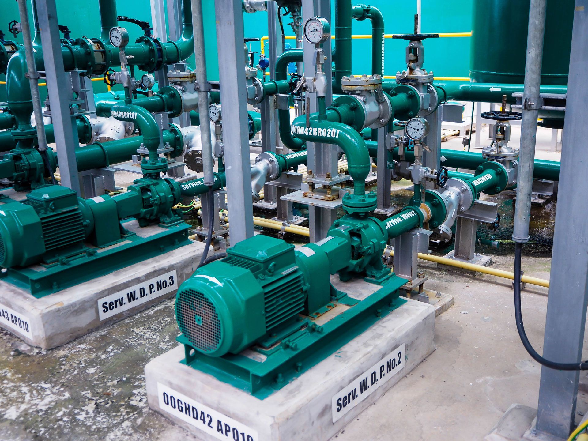Green industrial pumps and pipes in a machinery room, some with gauges.