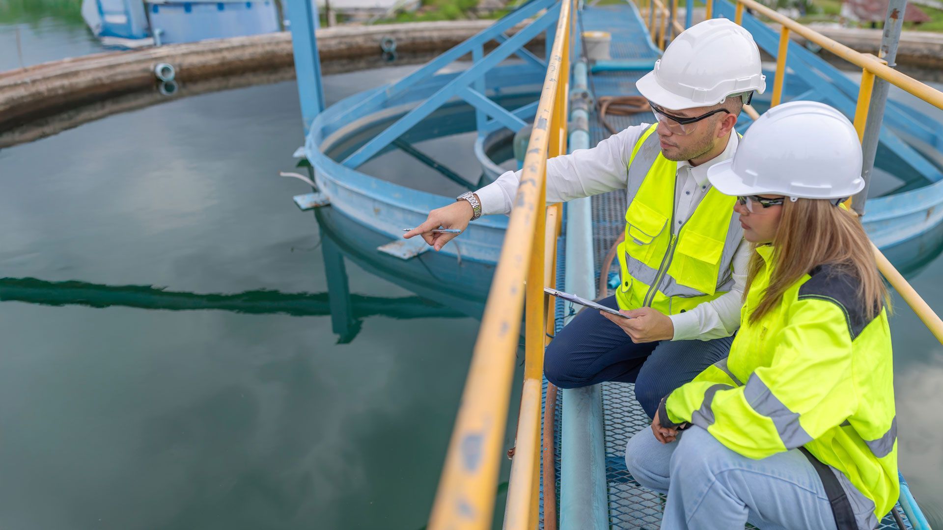 Two people in safety vests and hard hats inspecting water treatment facility.