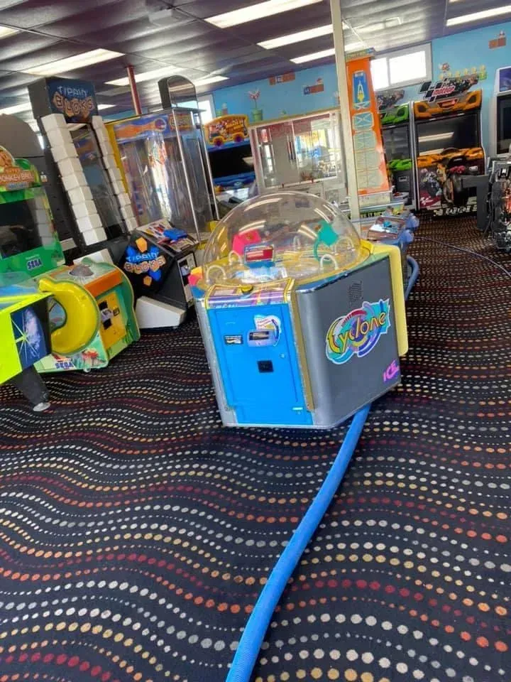 An arcade floor featuring a central claw machine with a blue base, surrounding various colorful game cabinets.