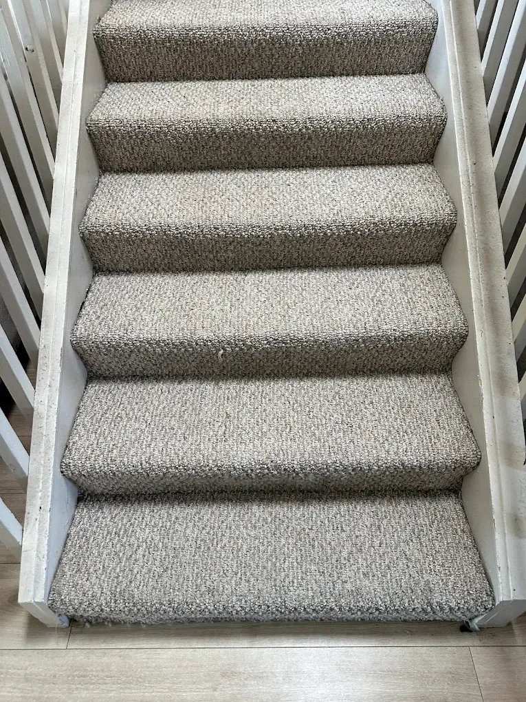 A set of six carpeted stairs with light gray and beige speckled carpeting, enclosed by white wooden side railings.
