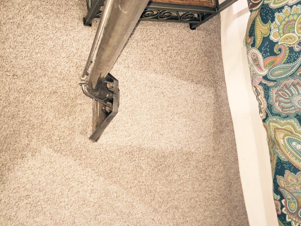 A carpet cleaning wand cleans a stripe of dirty beige carpet, showing the difference between cleaned and soiled areas.