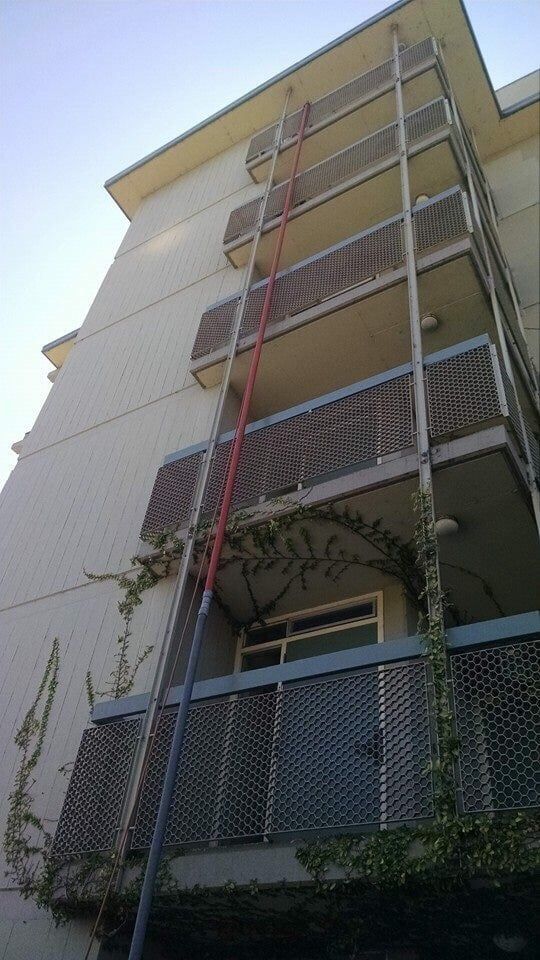 A low-angle view of a multi-story apartment building with stacked balconies and a red pole extending up the side.