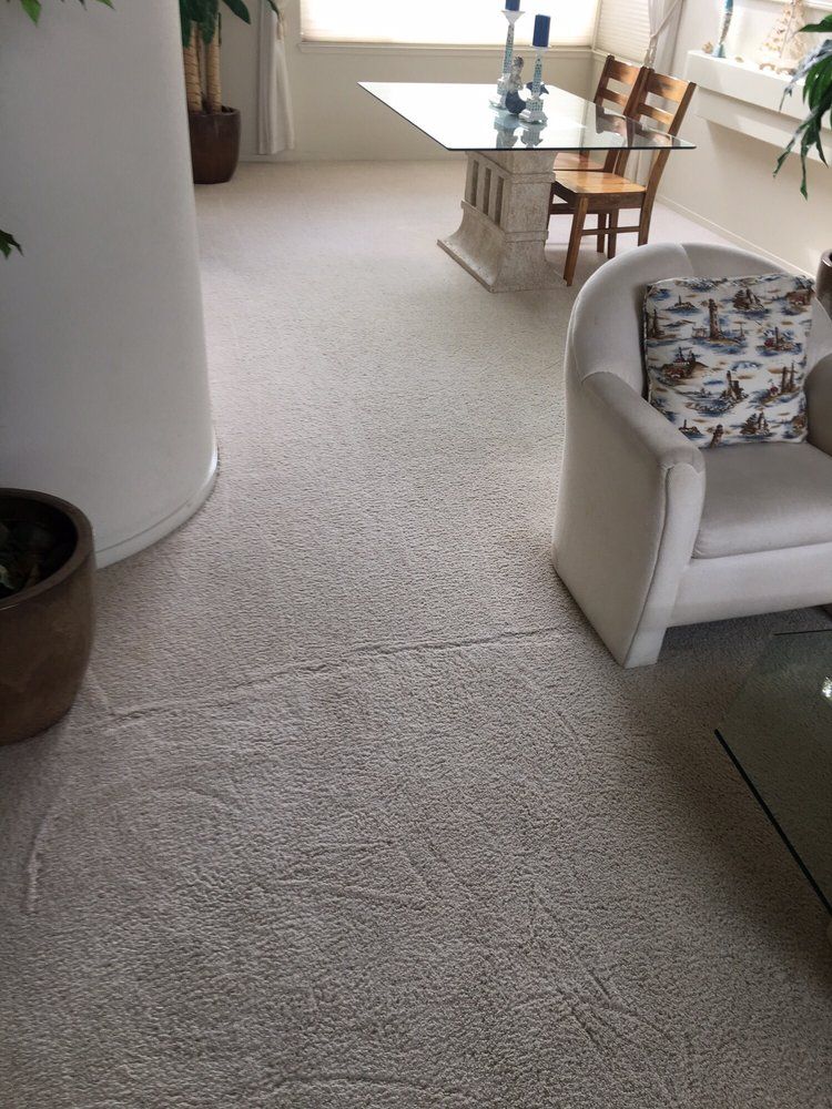 A cozy living space with light carpet, a beige armchair with a patterned pillow, and a glass-top dining table in the back.