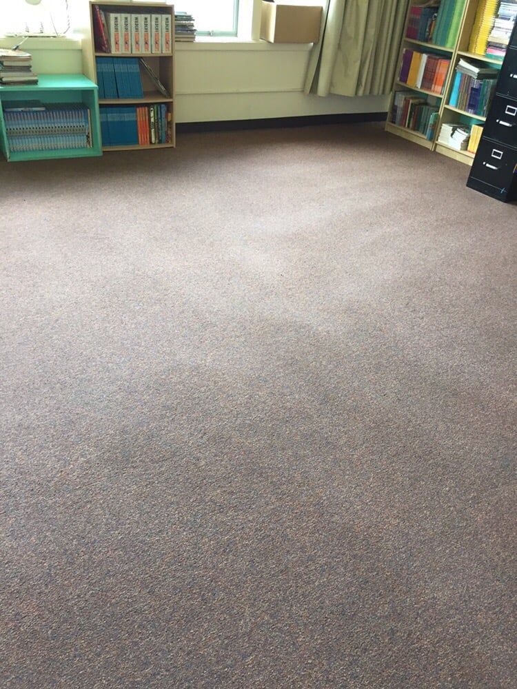 A room with tan carpet, a blue bookshelf on the left, and a wooden bookshelf with books on the right.