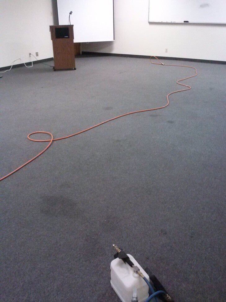 An orange extension cord snakes across a gray carpeted conference room floor leading toward a wooden podium.