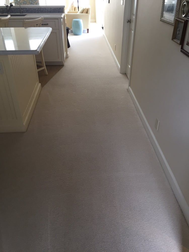A brightly lit indoor hallway with light-colored carpet leading past a kitchen island toward an open living area.