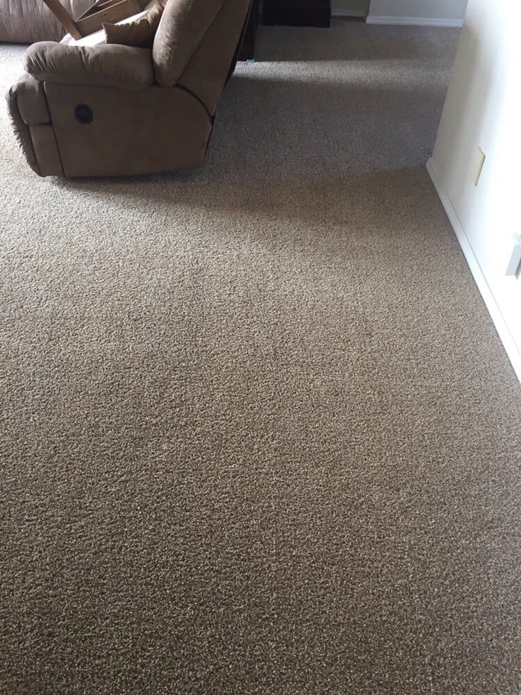 A partial view of a brown upholstered recliner sitting on beige, flecked wall-to-wall carpeting in a room.