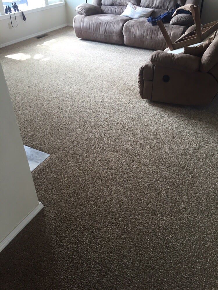 A living room with brown carpet, a brown sofa, and a recliner facing a window.