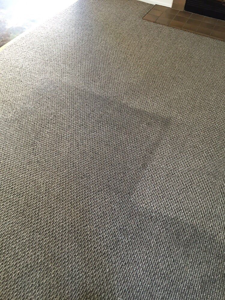 A top-down view of a textured, light-brown carpet showing a distinct square pattern imprinted from furniture.