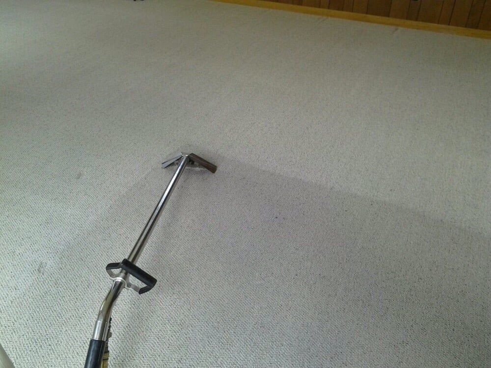 A metal carpet cleaning wand on light-colored carpet, showing a clean, dark path where the carpet has been washed.